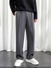 Model wearing men's charcoal baggy joggers with elastic waist and front crease paired with white sneakers and black top